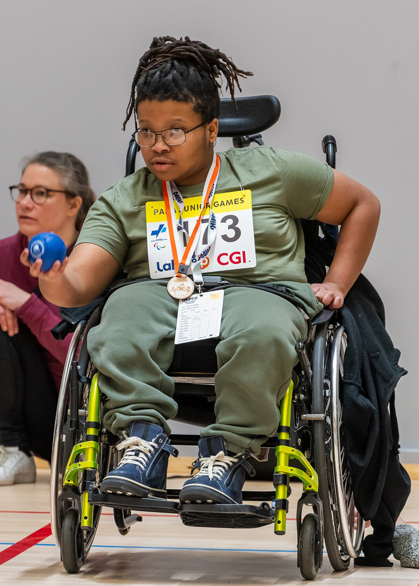 Pyörätuolia käyttävä tyttö heittää bocciapalloa.